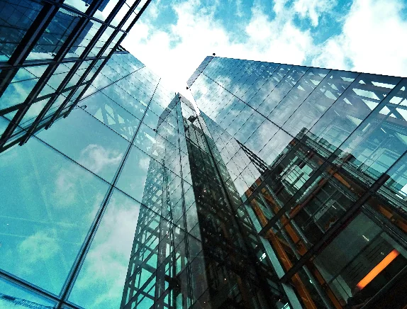 A glass office tower rising into a blue sky